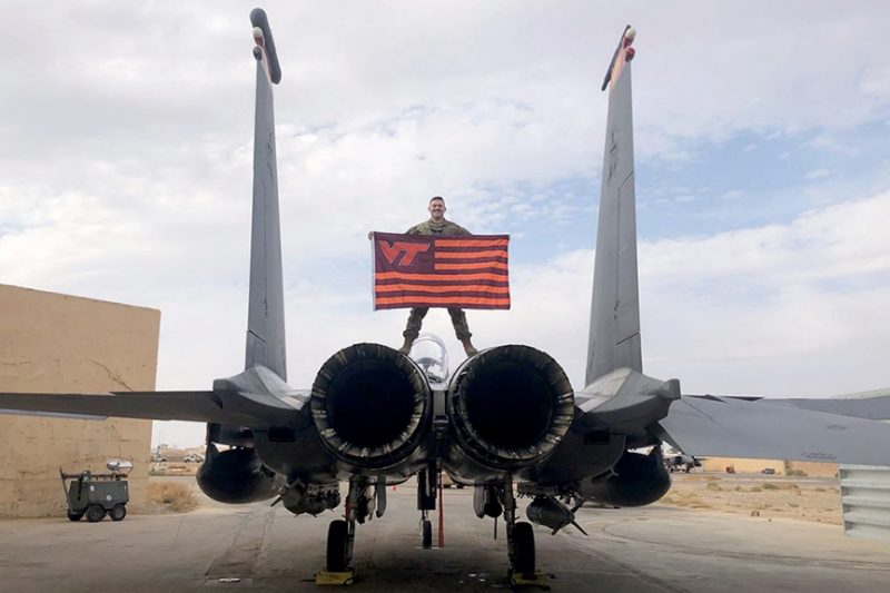 A Corps alumnus holds up a Virginia Tech flag while standing on an aircraft.