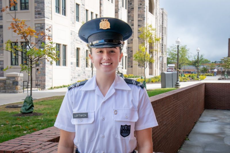 Cadet Leftwich stands in her uniform smiling in front of a Hokie stone building. 