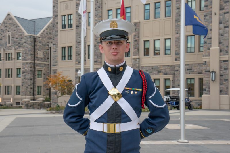 Cadet Waldron stands in his uniform smiling in front of a Hokie stone building. 