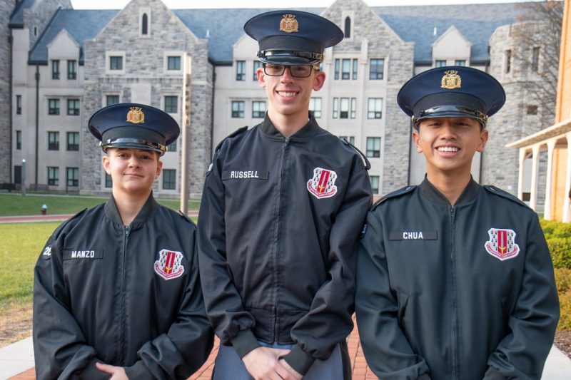 Cadets in uniform stand smiling with a Hokie Stone building in the background. 