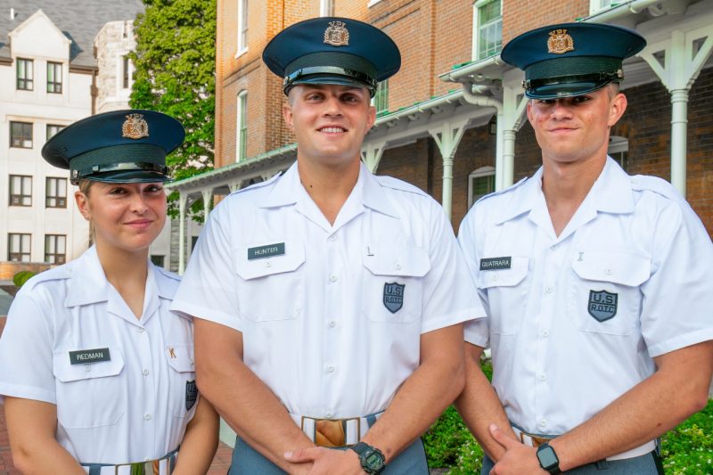 Cadets in white uniform shirts stand smiling in front of the historic brick of Lane Hall. 