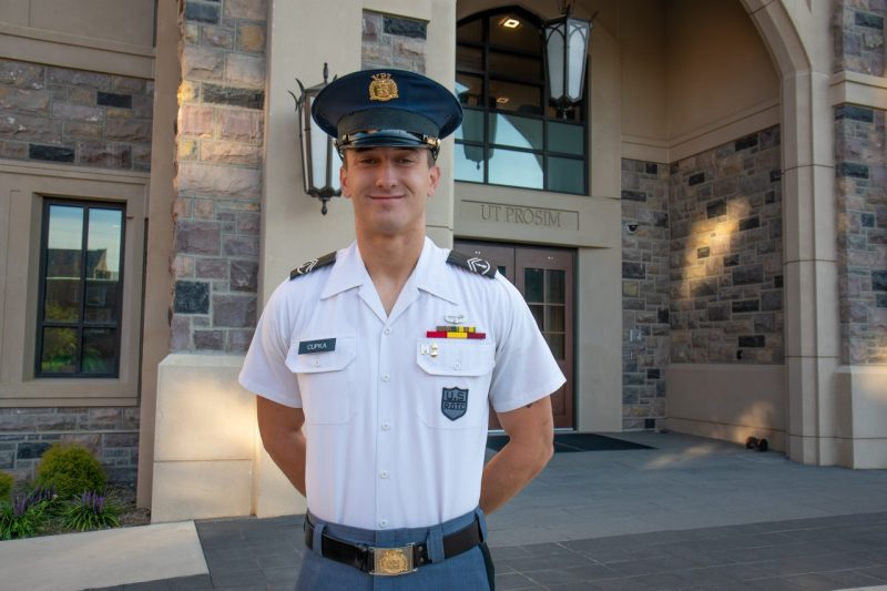 Cupka stands in uniform in front of a Hokie stone building while smiling.
