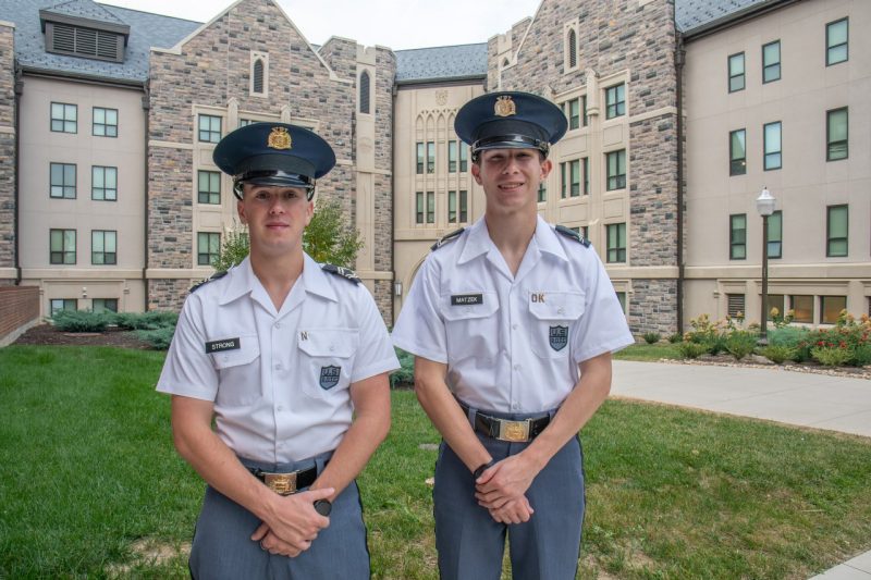 Strong and Matzek stand in uniform in front of a Hokie stone building while smiling. 