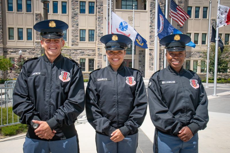  Cadets in uniform stand smiling in front of a Hokie stone building. 