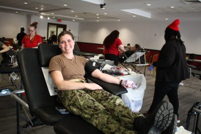 A student in uniform smiles at the camera while waiting for her blood donation to begin.