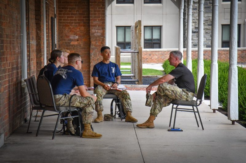 Sgt. Maj. Combs sits on the shaded porch of Lane Hall surrounded by cadets who are listening to him as he speaks.