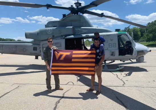 Hintz and Oberoi hold a VT flag in front of a military helicopter. Oberoi has a small child on his shoulders.