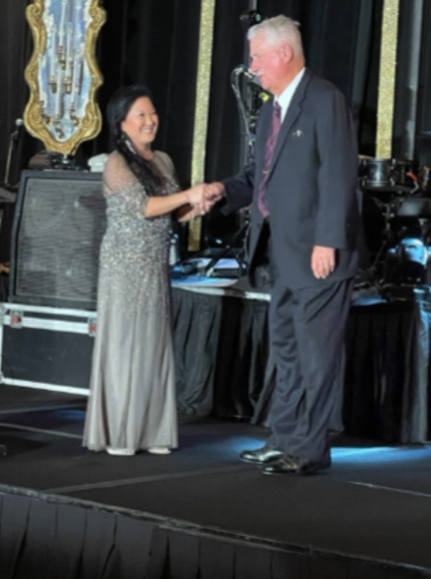 Mark stands on stage and shakes the hand of a woman who is smiling.