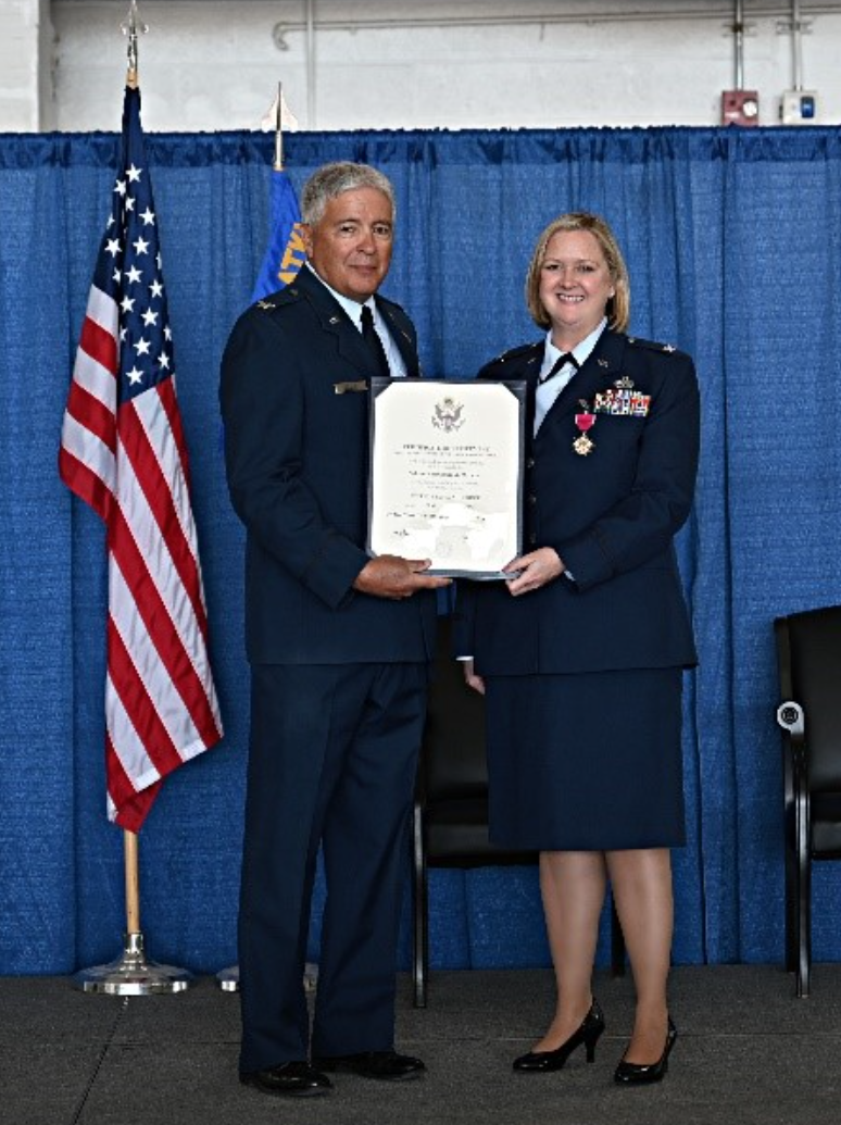 Hutson stands in her dress uniform holding a certificate with a man in uniform
