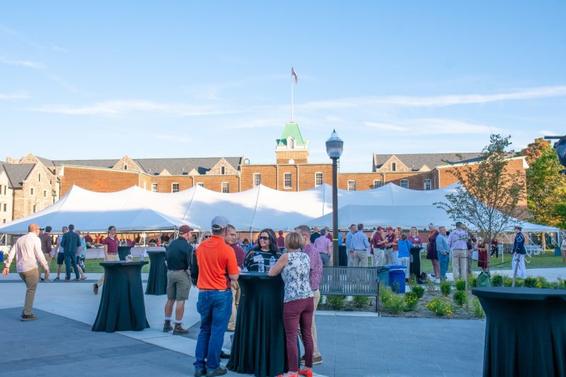 A crowd mingles around hightop tables and a large tent behind Lane Hall on Upper Quad