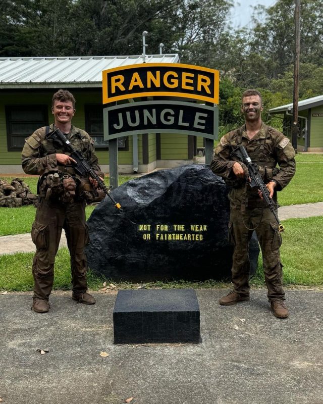 Two people stand in Army uniforms that are wet. They are smiling and standing by a sign that reads "Ranger Jungle Not for the weak or fainthearted"