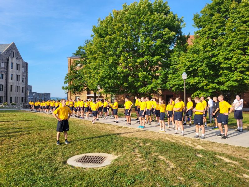 A large group of Navy midshipman stand in workout uniforms on Upper Quad.
