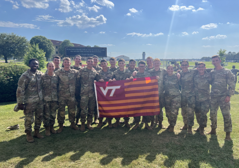 A large group of Air Force cadets stand in uniform arm in arm holding a striped VT flag.