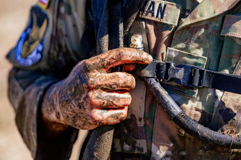 A closeup of a cadet's harm, hand, and uniform covered in mud.
