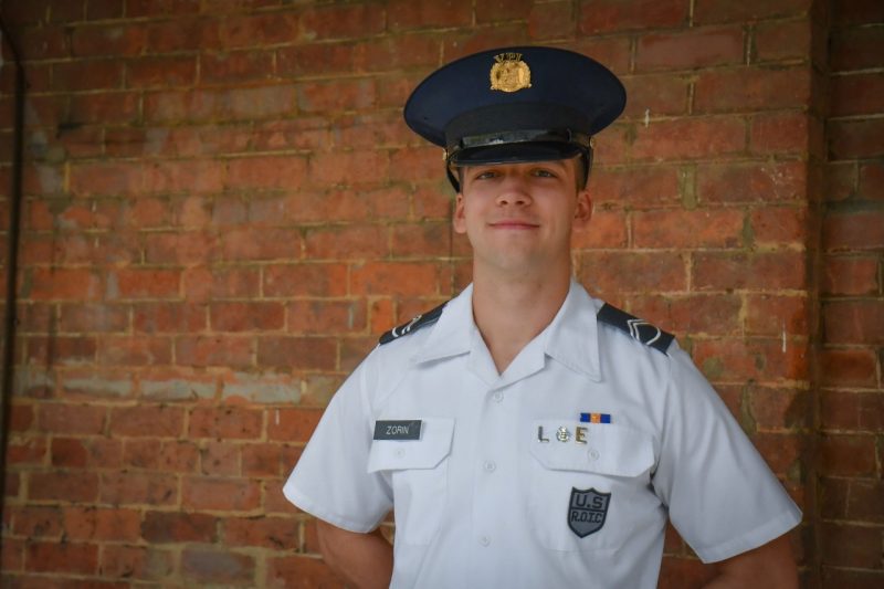 Cadet Zorin smiles and stands in uniform against the brick wall of Lane Hall.