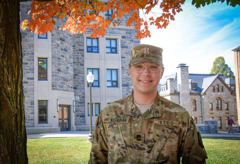 Cadet Nazarian stands in uniform smiling on Upper Quad with Hokie stone and fall leaves in the background.