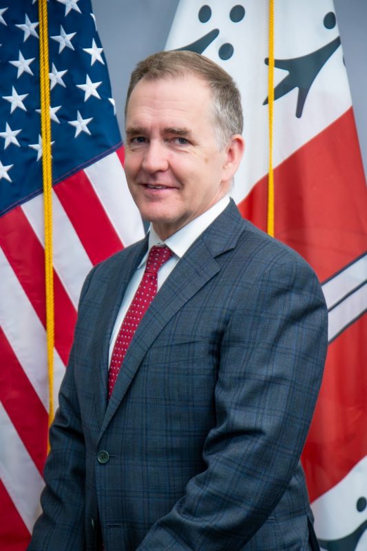 Portrait of Brian Callsen in front of the Corps of Cadets and American flags