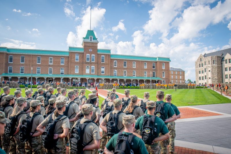 Large groups of new cadets and their training cadre stand in formation on the sidewalks in front of Lane Hall. 
