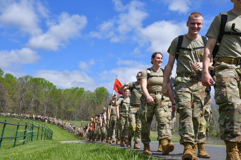 First-year cadets walk in a long single line down a road during Caldwell March. There are lots of smiles and the cadets are in their camouflage uniforms.