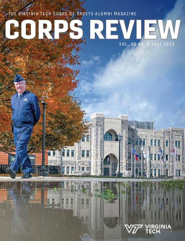 The new Corps Leadership and Military Science Building sits in the background while Maj. Gen. Fullhart walks in his uniform in the foreground. Bright orange leaves from trees on Upper Quad are in the background and the whole scene is reflected in a puddle in the foreground.