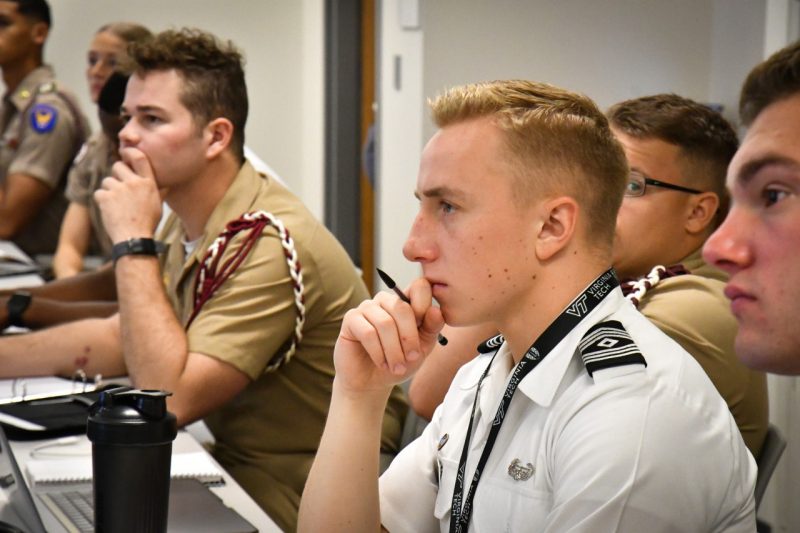 A Virginia Tech cadet watches a speaker closely. Other cadets are also paying attention in the background.