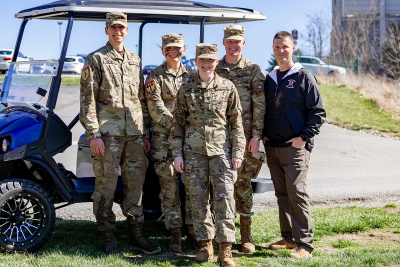 The group stands in front of a golf cart near the obstacle course and smiles at the camera.
