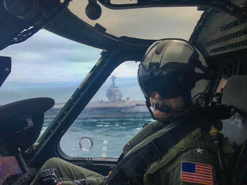 Steffen pilots a helicopter with an aircraft carrier in the background