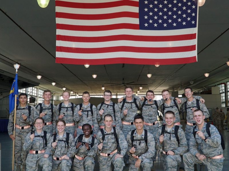 A field training group poses for a picture underneath a large American flag. Cadet Margaret McConville ’22  is at bottom left.