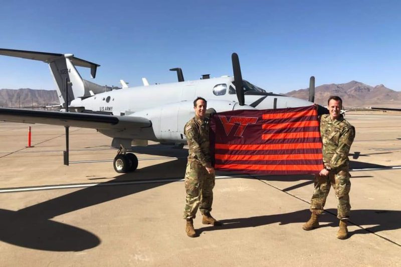 Capt. Ben Isaacs I’12 (left) and Capt. Danny Deardorff E’15 hold a Virginia Tech flag in front of  an RC-12X Guardrail Common Sensor aircraft.