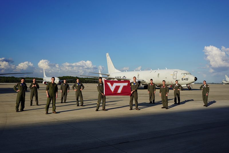 Eleven Hokies stand on the tarmac in front of an aircraft.