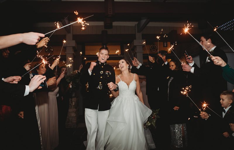 2nd Lt. Clark Shotwell ‘19 (at left) and 2nd Lt. Lauren (Zuchowski) Shotwell ‘20 (at right) walk through a crowd holding sparklers during their wedding.