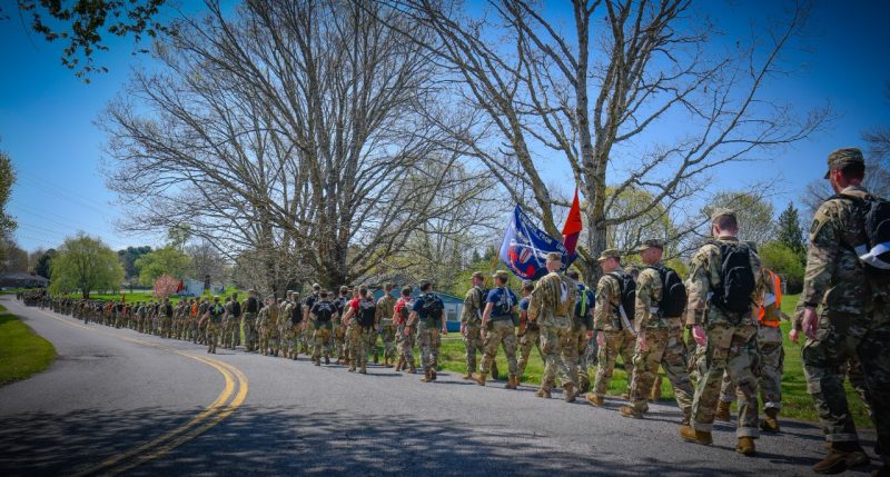 Cadets walk in a long line down a curved road with blooming trees in the background during the spring 2022 Caldwell March