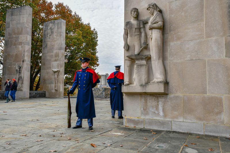 Two cadets in dress unforms at capes stand guard at the Ut Prosim Pylon.